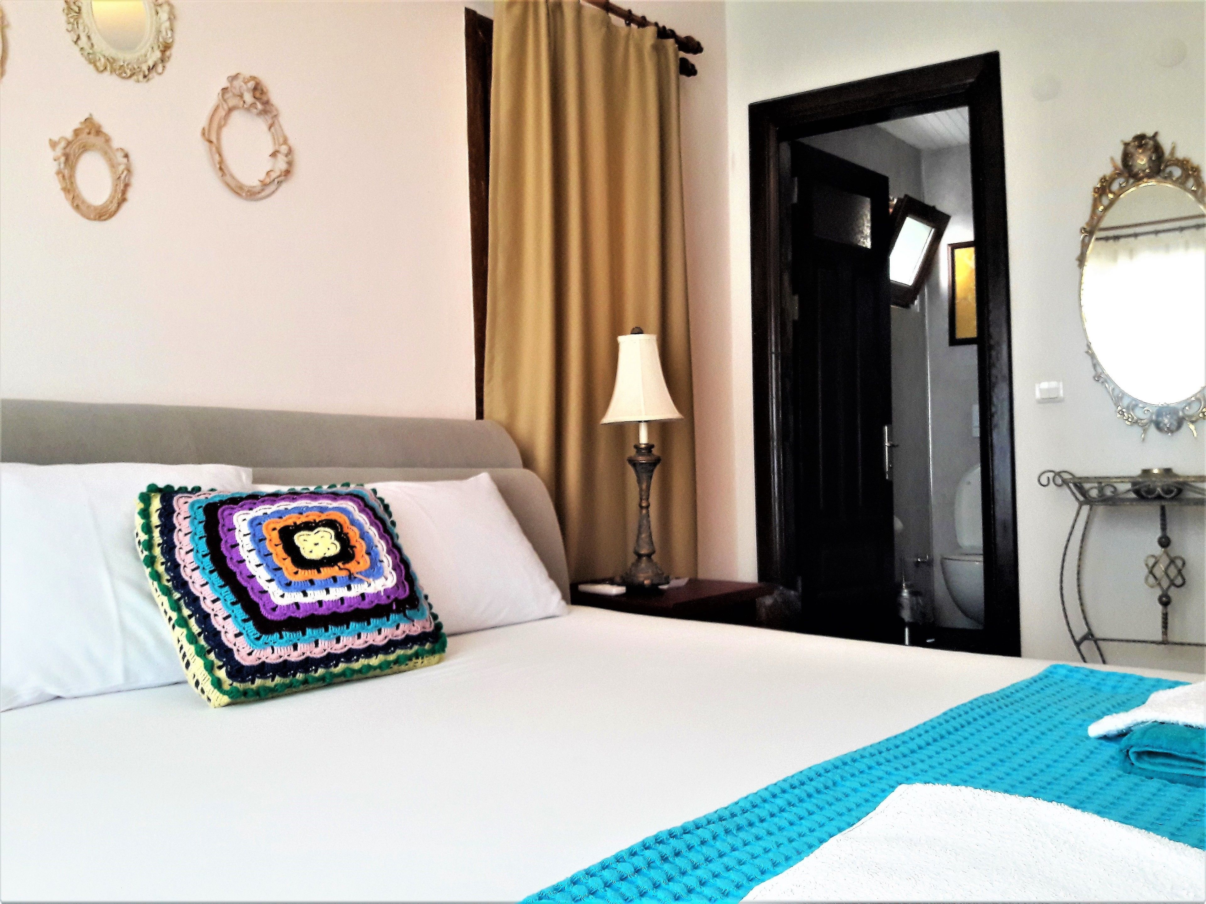 Habitación de hotel con una cama, un cojín de crochet colorido, una lámpara y un espejo en la pared.