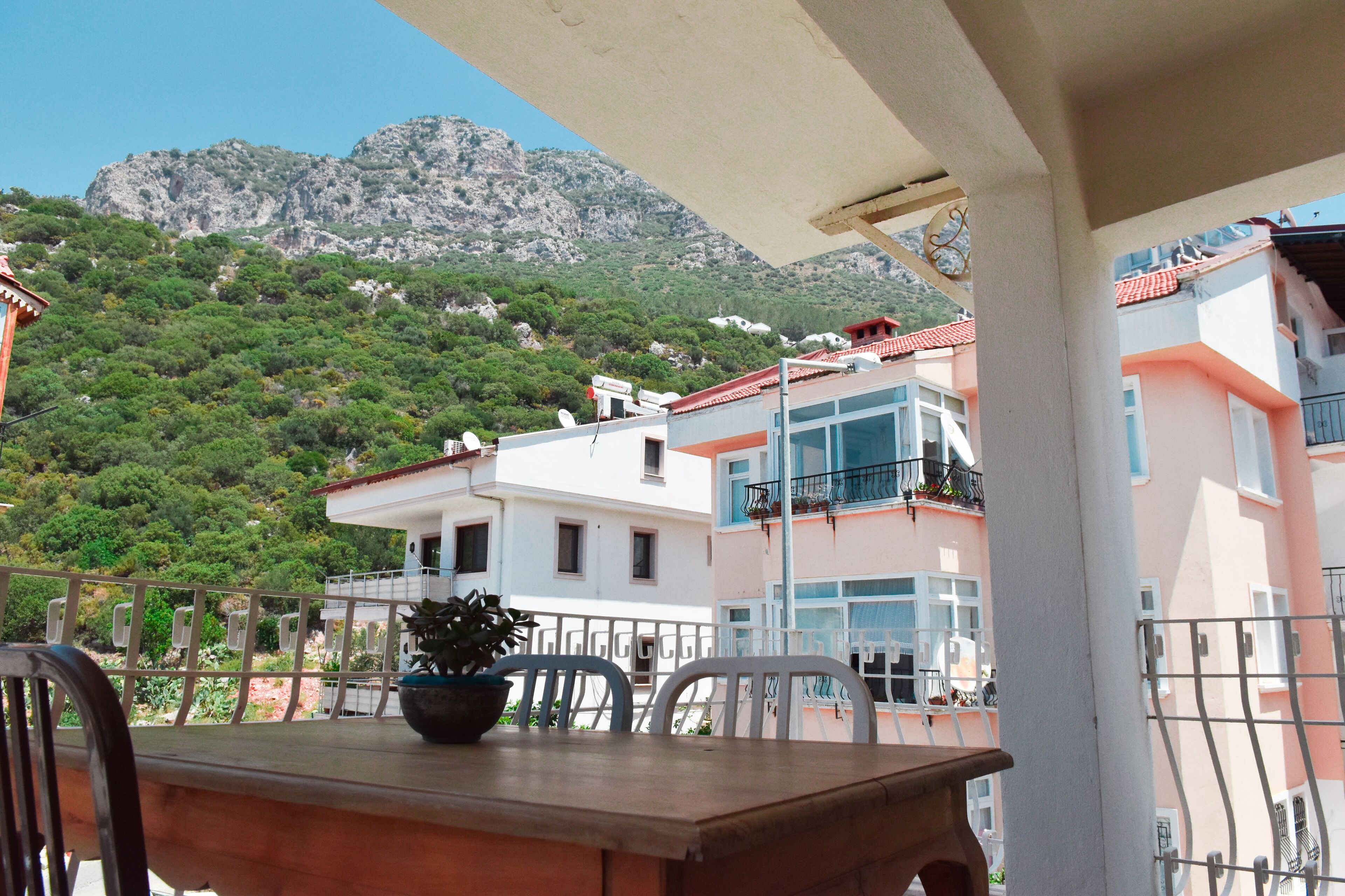 A terrace with a table and chairs, overlooking a hillside with buildings and a mountain.