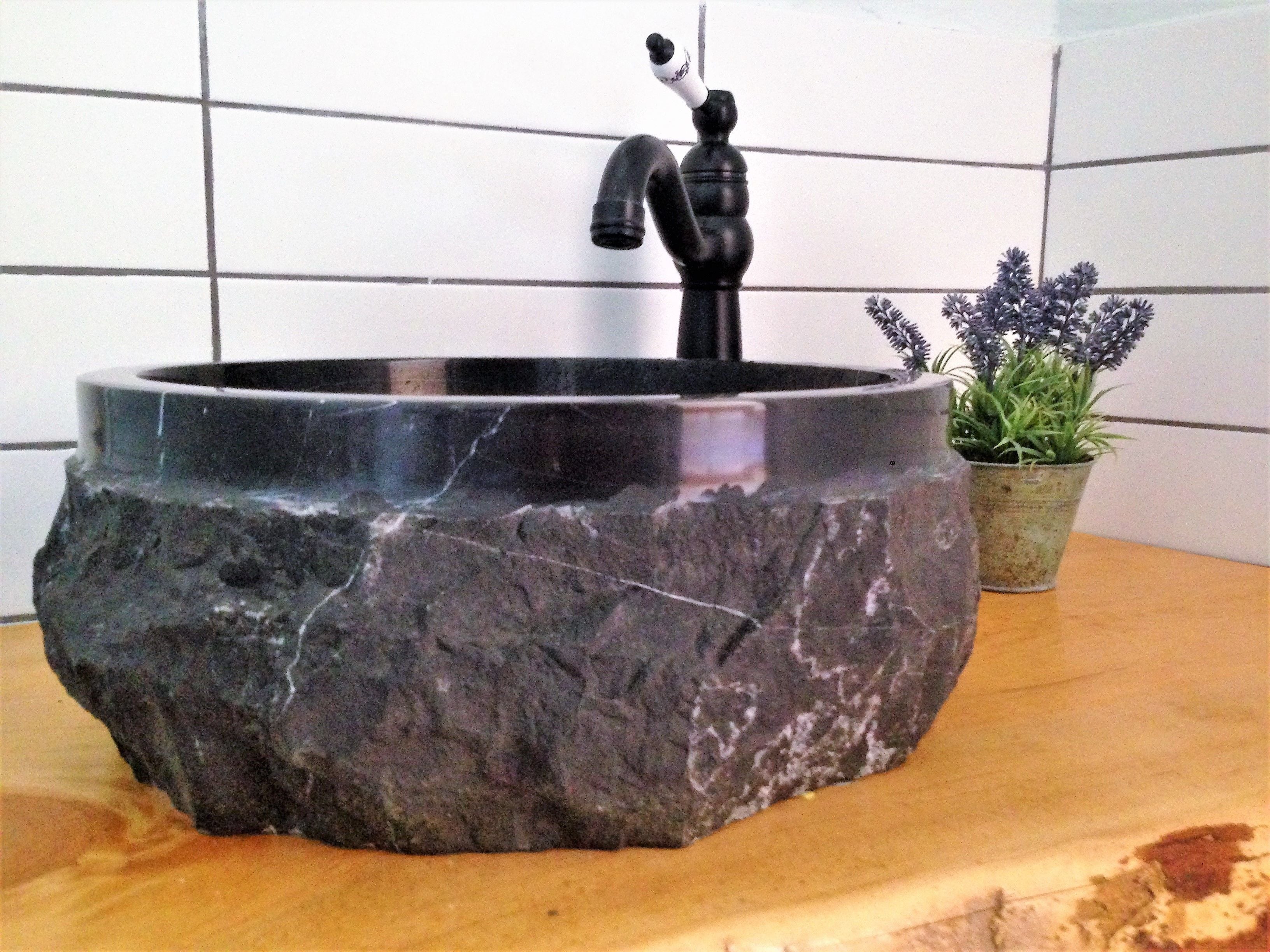 Een badkamer met een zwart marmeren wastafel, een kraan en een pot met een plant.