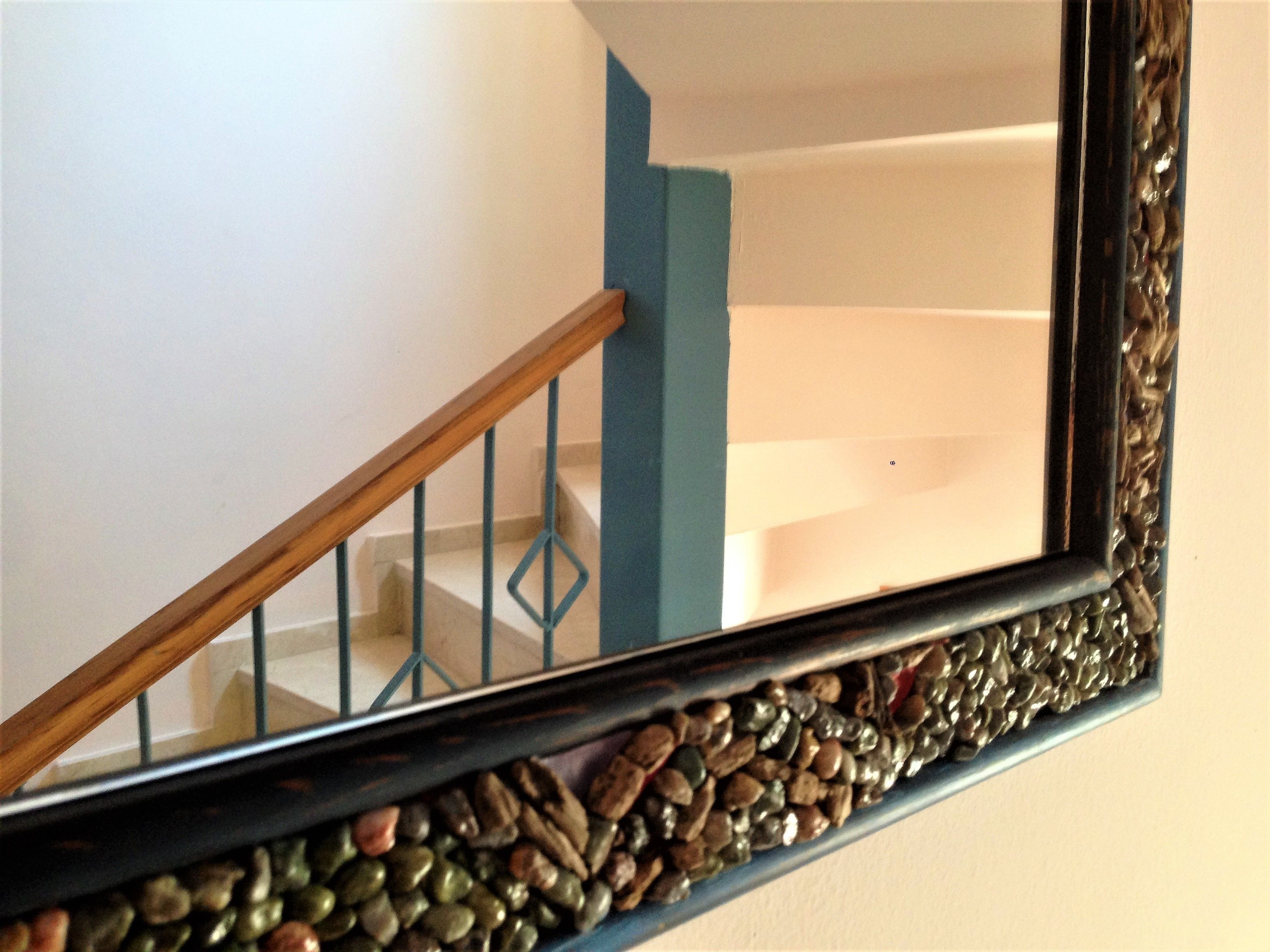 A mirror with a decorative frame reflecting a staircase with a wooden handrail and blue accents.