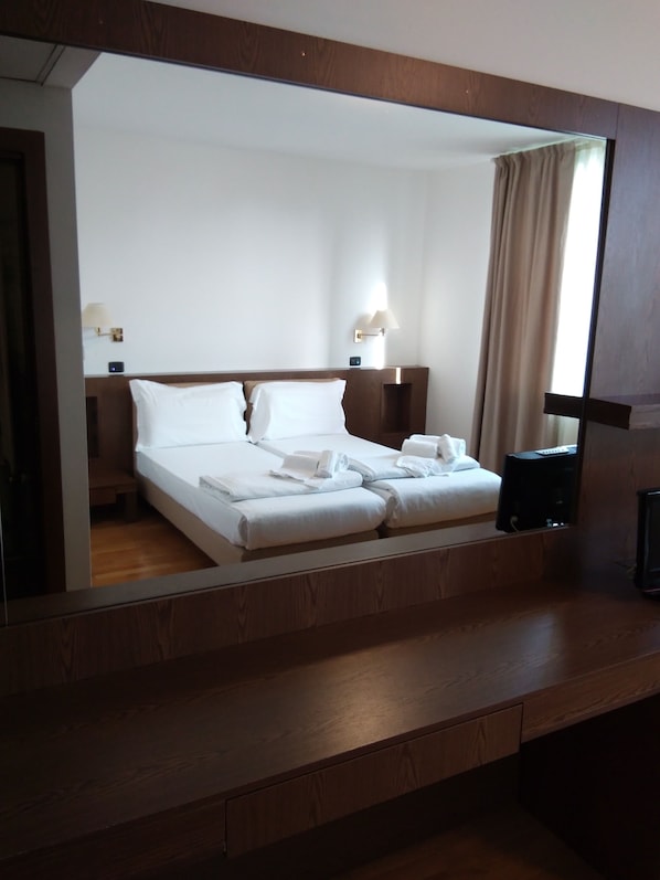 Una habitación de hotel con cama, mesitas de noche, lámpara y un espejo grande.