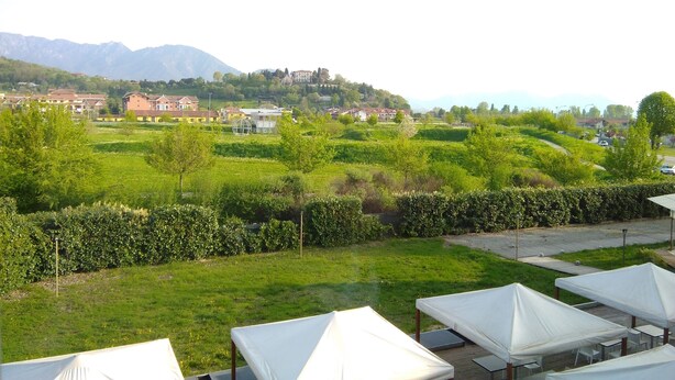 A view of a hotel with outdoor seating areas and a backdrop of a green landscape with buildings and mountains. - Hotel Cavalieri Pinerolo (Pinerolo)
