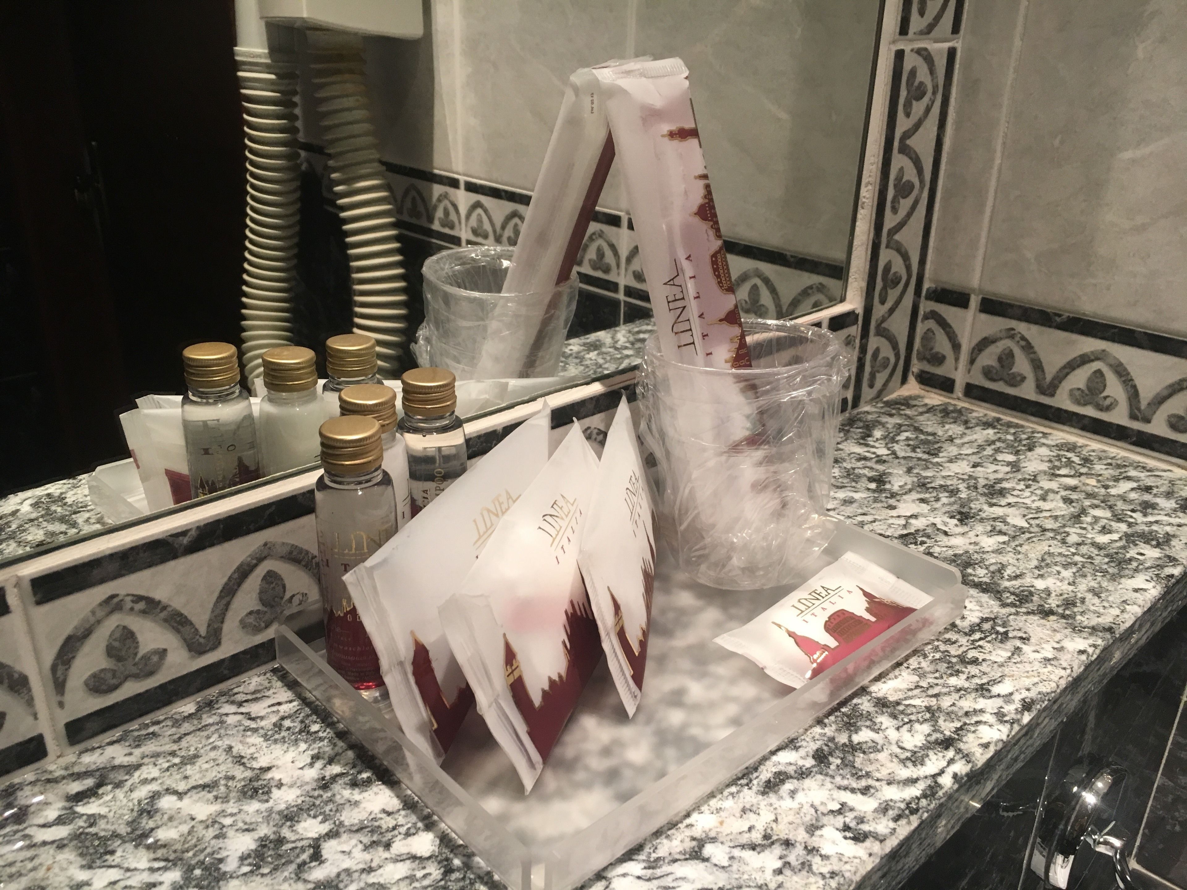 Una encimera de baño con artículos de aseo, un vaso de agua y una caja de pañuelos.