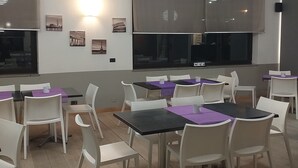 A dining area with tables and chairs, a large window, and wall-mounted lights. - Hotel Cavalieri Pinerolo (Pinerolo)