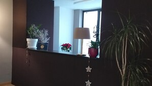 A reception area with a dark wall, a window, and a potted plant. - Hotel Cavalieri Pinerolo (Pinerolo)