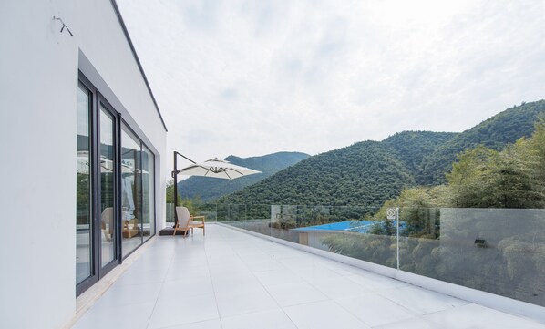 A modern balcony with a glass railing, a chair, and a large umbrella.