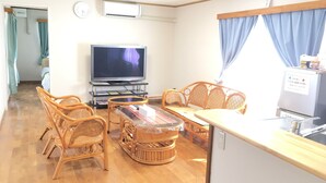 A living room with a television, wicker furniture, a glass coffee table, and a kitchen area with a refrigerator. - Pension Ishigaki Tomatamatsu (Ishigaki)