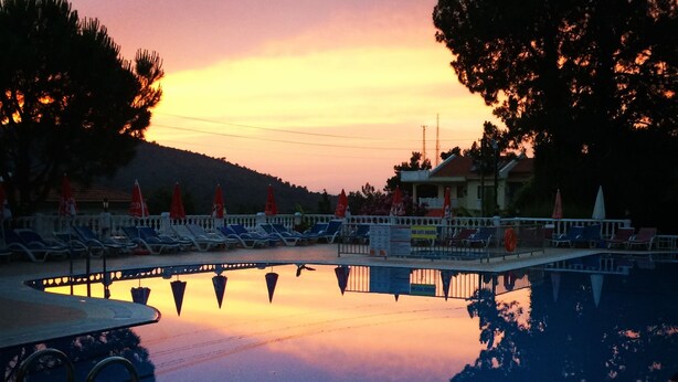 A swimming pool with lounge chairs and umbrellas, surrounded by trees and buildings.