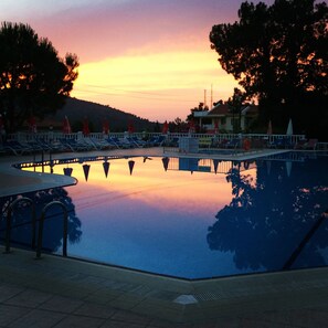 A swimming pool with lounge chairs and umbrellas, surrounded by trees and buildings. - Hotel Leytur (Fethiye)