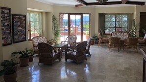 A spacious living area with wicker furniture, a glass-top coffee table, and potted plants.