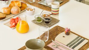 Una mesa de desayuno con diferentes alimentos y bebidas, un mantel blanco y un camino de mesa de mimbre.