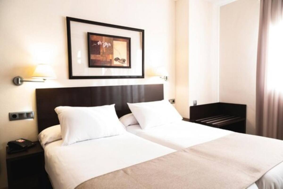 Quarto de hotel com duas camas, um quadro na parede e uma mesa de cabeceira com abajur.