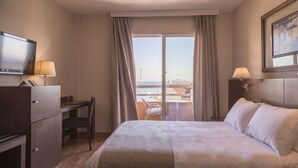 Hotellihuone, jossa on sänky, työpöytä, tuoli, televisio ja ikkuna, jossa on verhot.