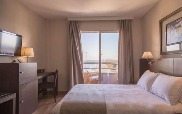 Una habitación de hotel con cama, escritorio, silla, televisión y ventana con cortinas.
