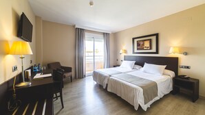 Hotellihuone, jossa on sänky, työpöytä, tuoli, televisio ja ikkuna, jossa on verhot.