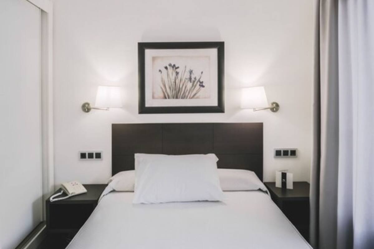 Quarto de hotel com cama, abajures, telefone e um quadro na parede.