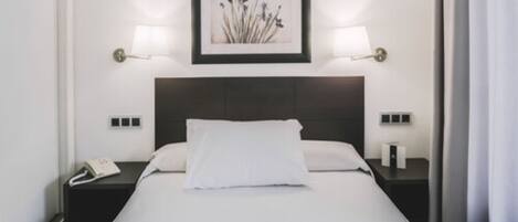 A hotel room with a bed, bedside lamps, a phone, and a framed picture on the wall.