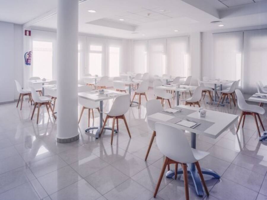 A spacious, modern conference room with white tables and chairs, large windows, and a clean, minimalist design.