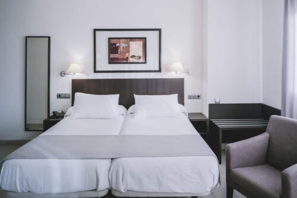 Quarto de hotel com cama de casal, duas mesas de cabeceira, uma cadeira, um espelho grande e um quadro na parede.