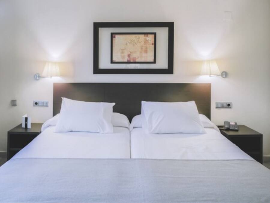 A double bed with white linens, two bedside tables with lamps, and a framed picture above the bed.