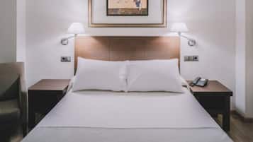 Una habitación de hotel con una cama, dos mesitas de noche, una silla, un cuadro enmarcado en la pared y una lámpara sobre cada mesita de noche.