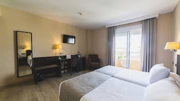 A hotel room with a bed, desk, chair, and a balcony with curtains.