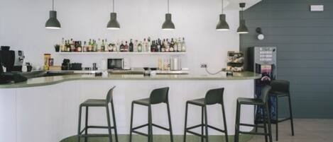 Una zona de bar con mostrador blanco, cuatro taburetes y lámparas colgantes.