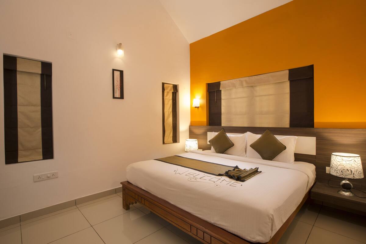A hotel room with a large bed, a nightstand with a lamp, and a framed picture on the wall.