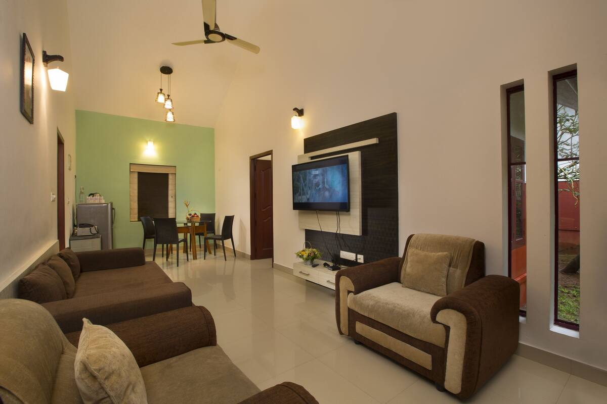 A modern living room with a flat-screen TV, sofas, a dining area, and a ceiling fan.