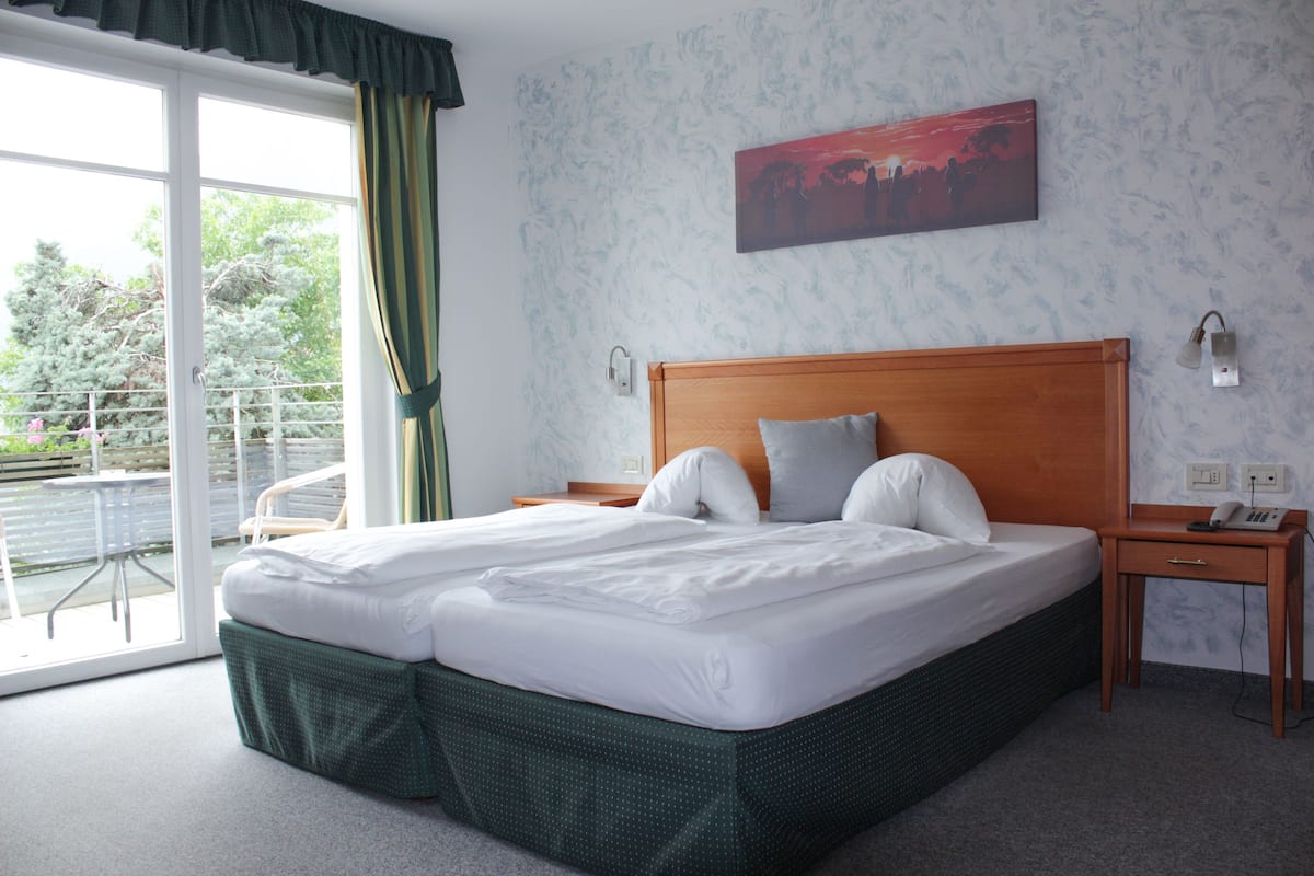 A hotel room with a large bed, a wooden headboard, a nightstand, a telephone, and a painting on the wall.