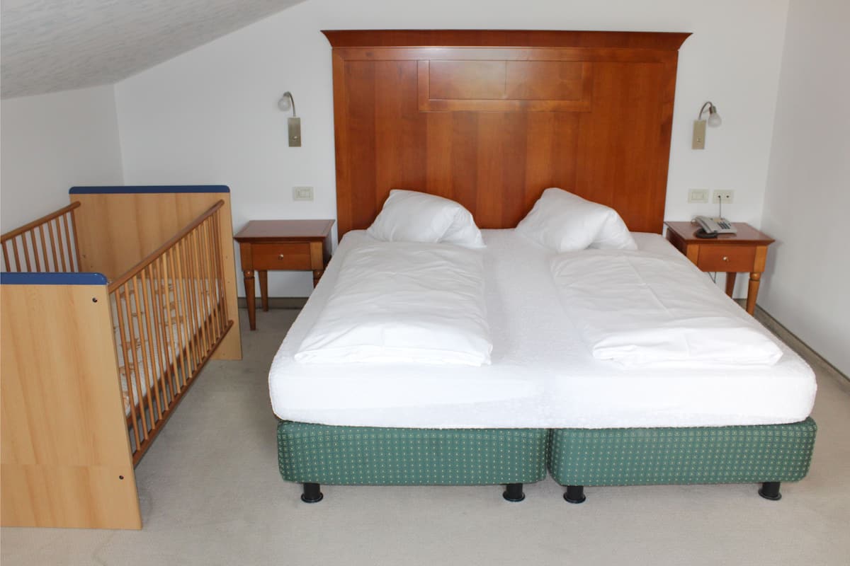 A double bed with a wooden headboard, two bedside tables, and a wooden crib.