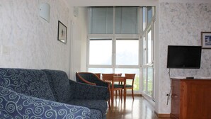 A living room with a patterned sofa, a dining table with chairs, a television, and a window with blinds. - Hotel Tannerhof (Schenna)