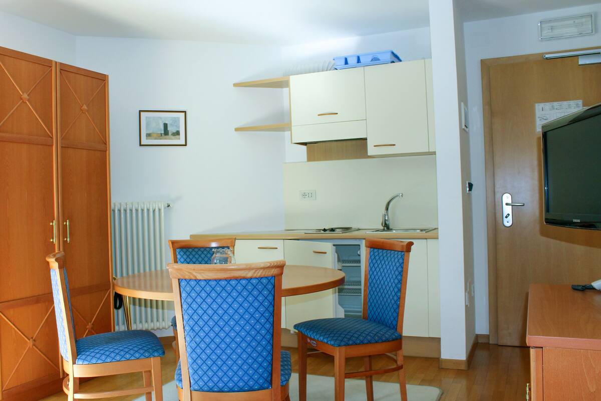 A compact kitchen with a dining area, wooden cabinets, a radiator, and a television.