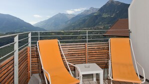A balcony with two orange lounge chairs, a small table, and a view of mountains. - Hotel Tannerhof (Schenna)