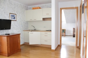 Una cocina compacta con armarios blancos, una encimera de madera y un televisor integrado.