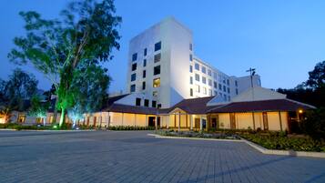 A modern hotel with a central tower and two wings, featuring a paved courtyard and landscaped gardens.