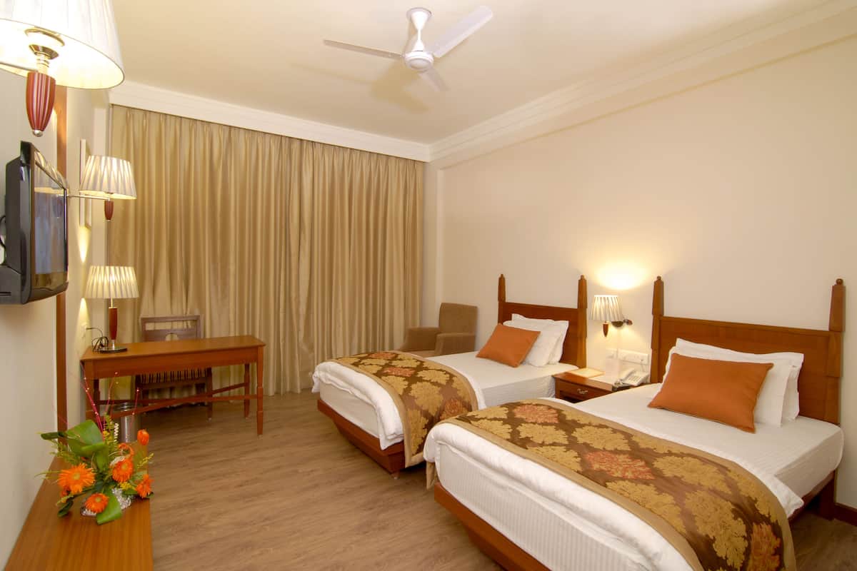 A hotel room with two beds, a desk, a chair, a TV, and a ceiling fan.