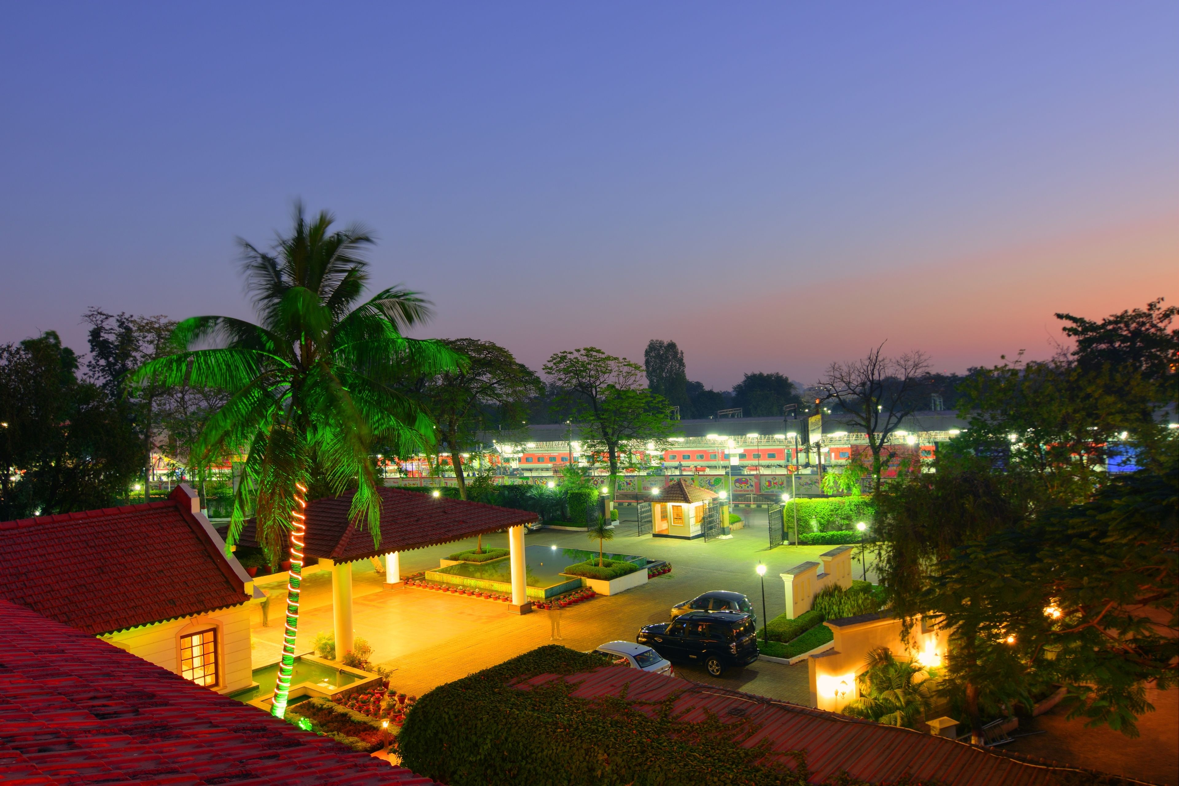A hotel with a red-tiled roof, a covered outdoor area with a palm tree, and a parking lot with cars.