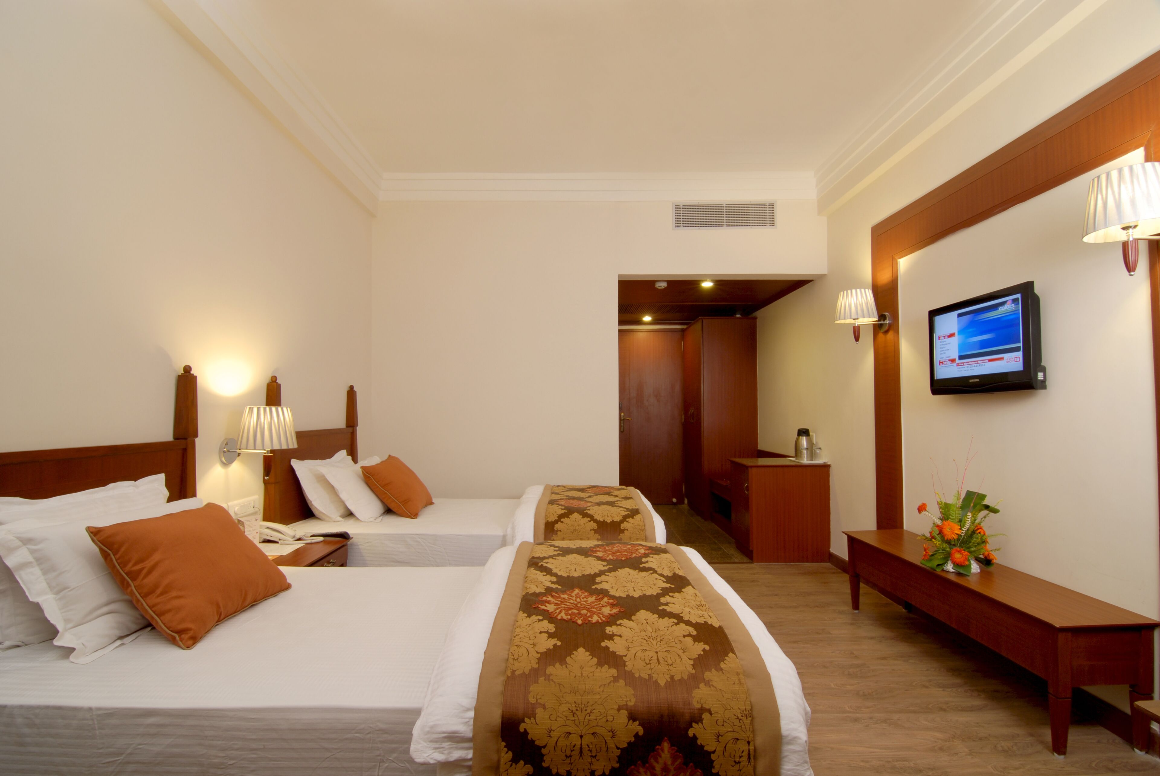 A hotel room with two beds, a TV, a desk, and a bench.