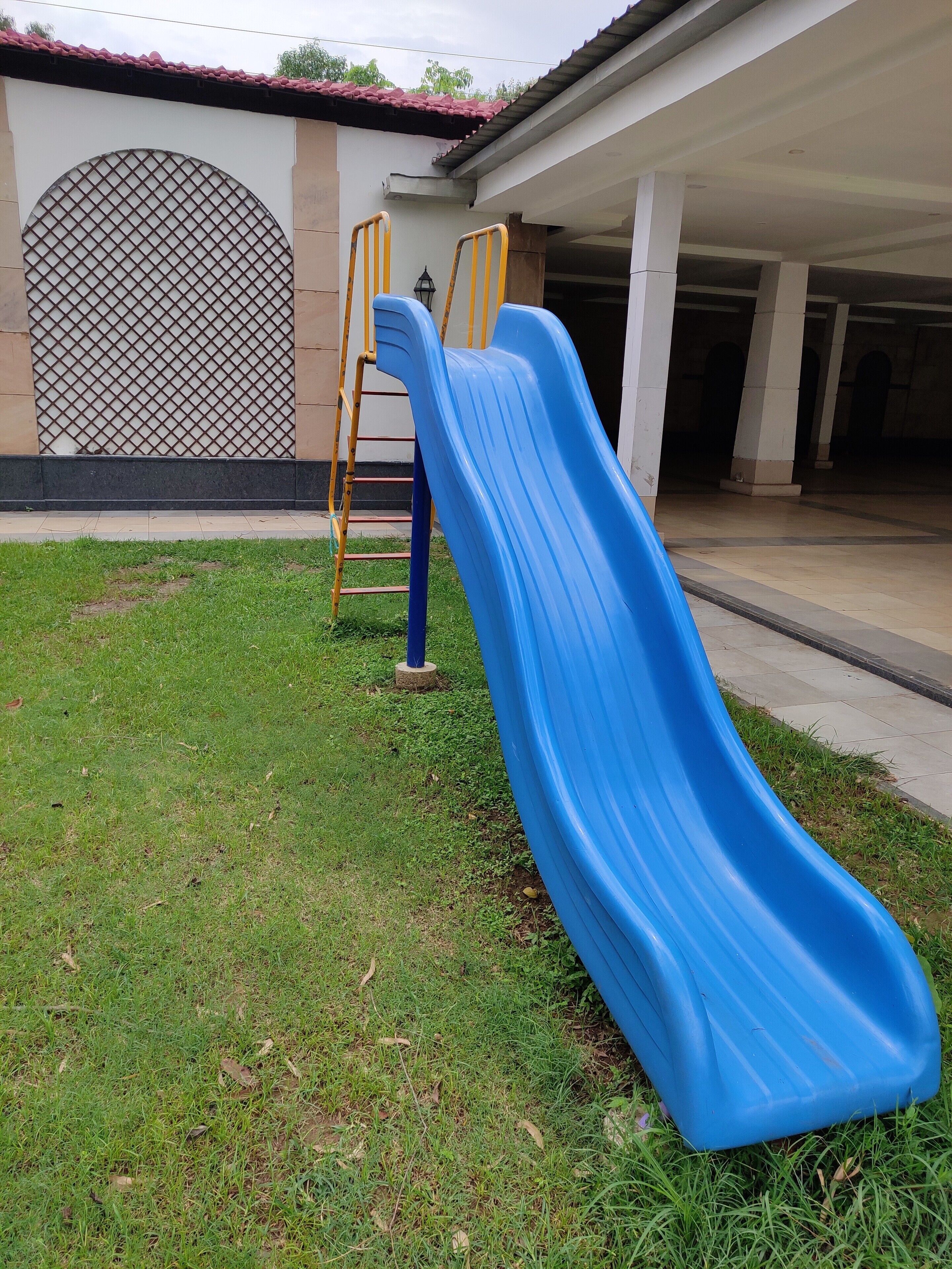 A blue slide in a grassy area with a building in the background.