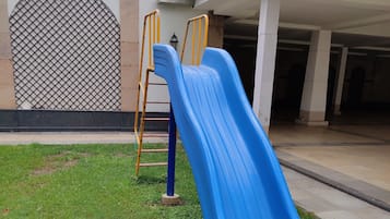 A blue slide in a grassy area with a building in the background.