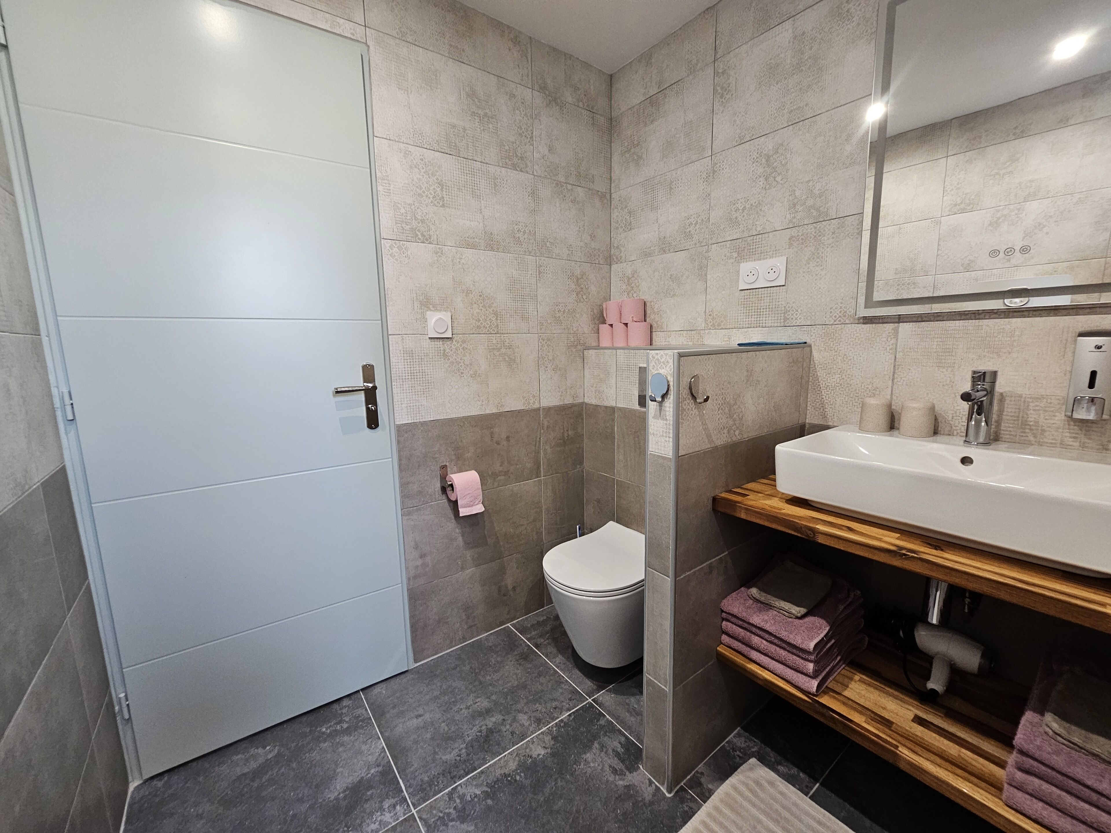 Un baño moderno con cabina de ducha, inodoro y lavabo con estante de madera.