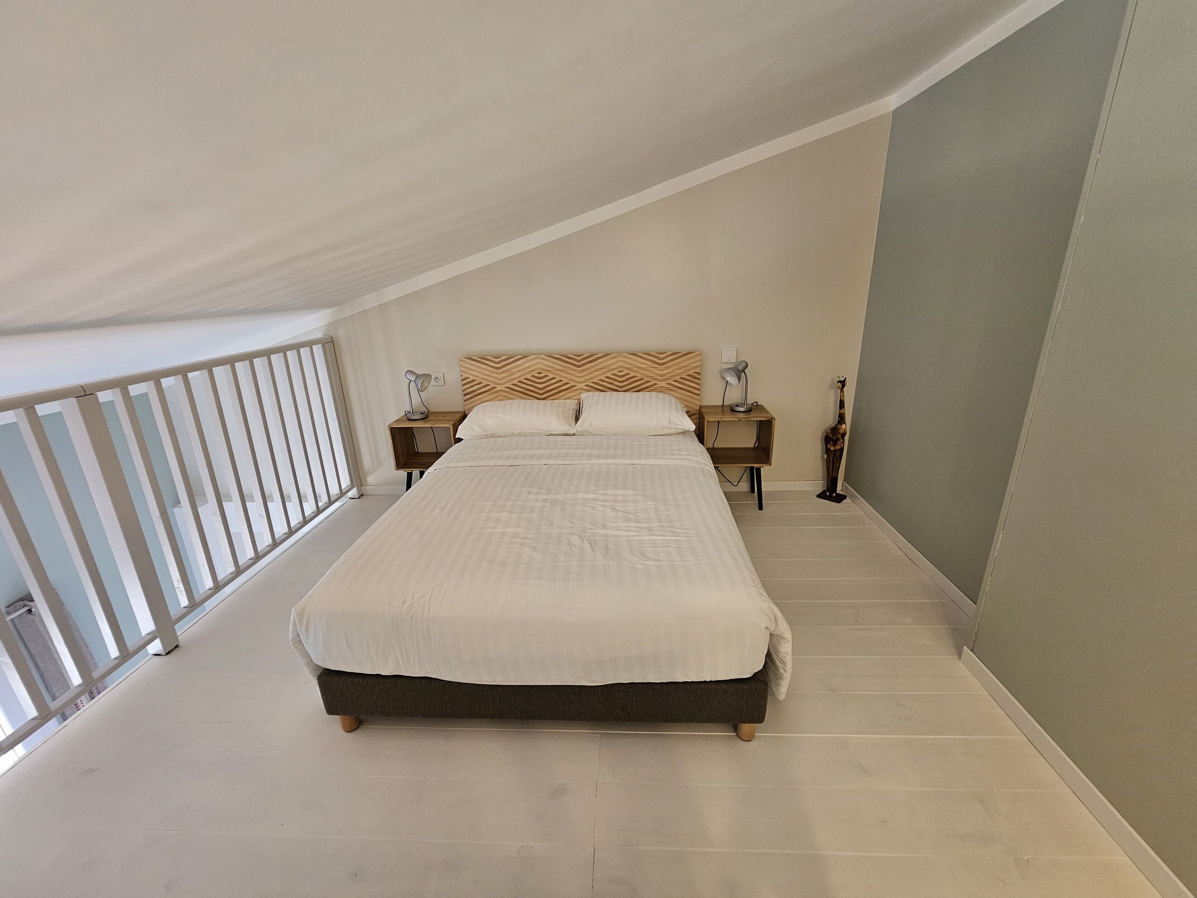 Un dormitorio con una cama grande, dos mesitas de noche con lámparas, un cabecero de madera y vistas al balcón.