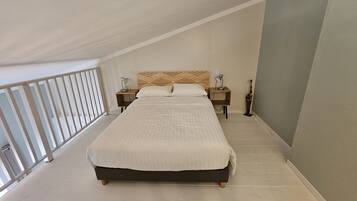 Un dormitorio con una cama grande, dos mesitas de noche con lámparas, un cabecero de madera y vistas al balcón.