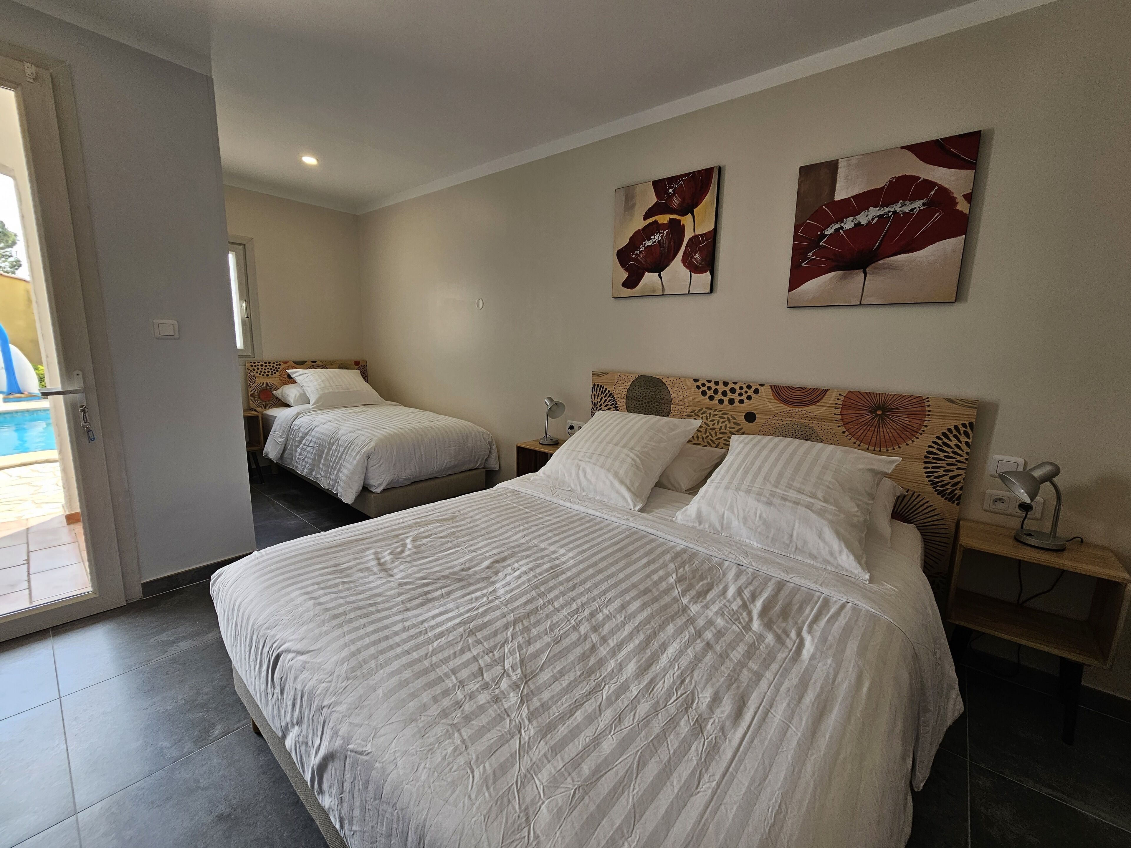 A hotel room with two beds, a wooden headboard, a nightstand with a lamp, and artwork on the wall.