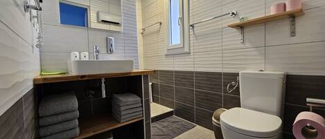 Un baño moderno con lavamanos, inodoro y zona de ducha.