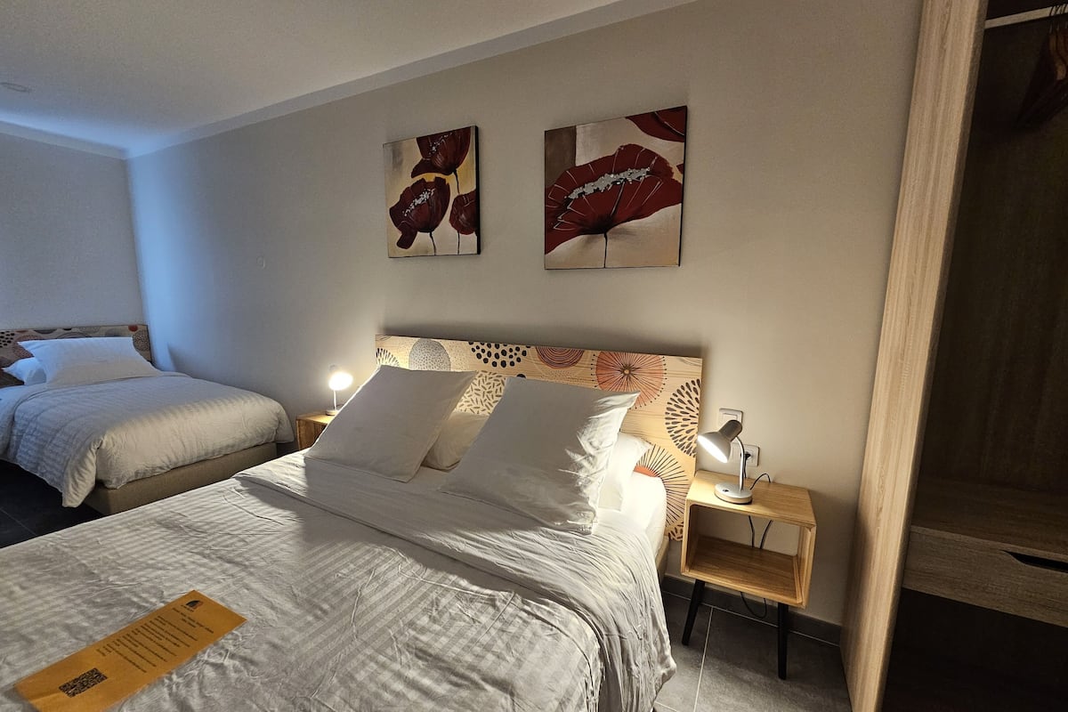Een hotelkamer met twee bedden, een houten hoofdbord, een nachtkastje met een lamp en twee kunstwerken aan de muur.