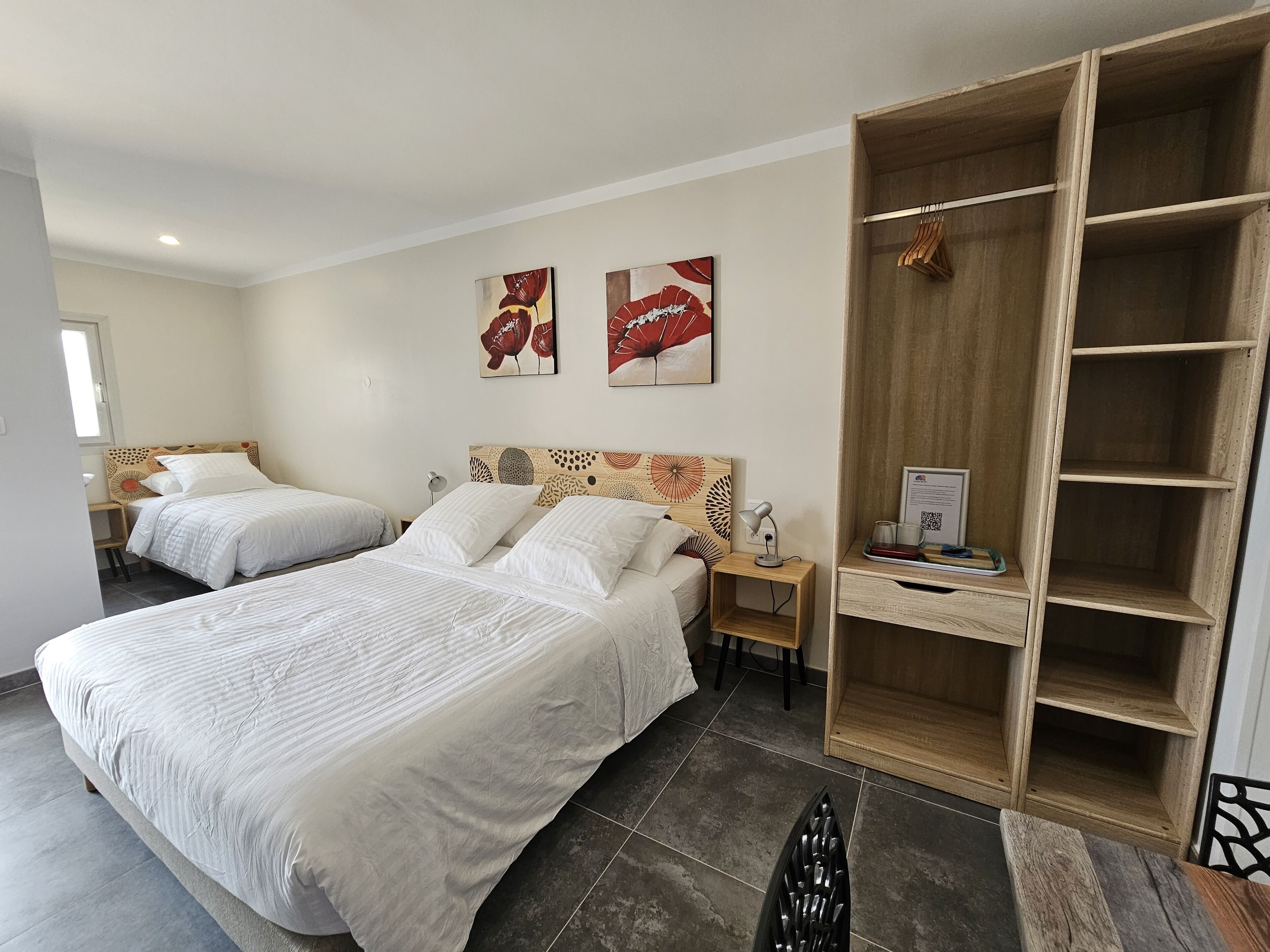A hotel room with two beds, a wooden wardrobe, a desk with a lamp, and artwork on the wall.