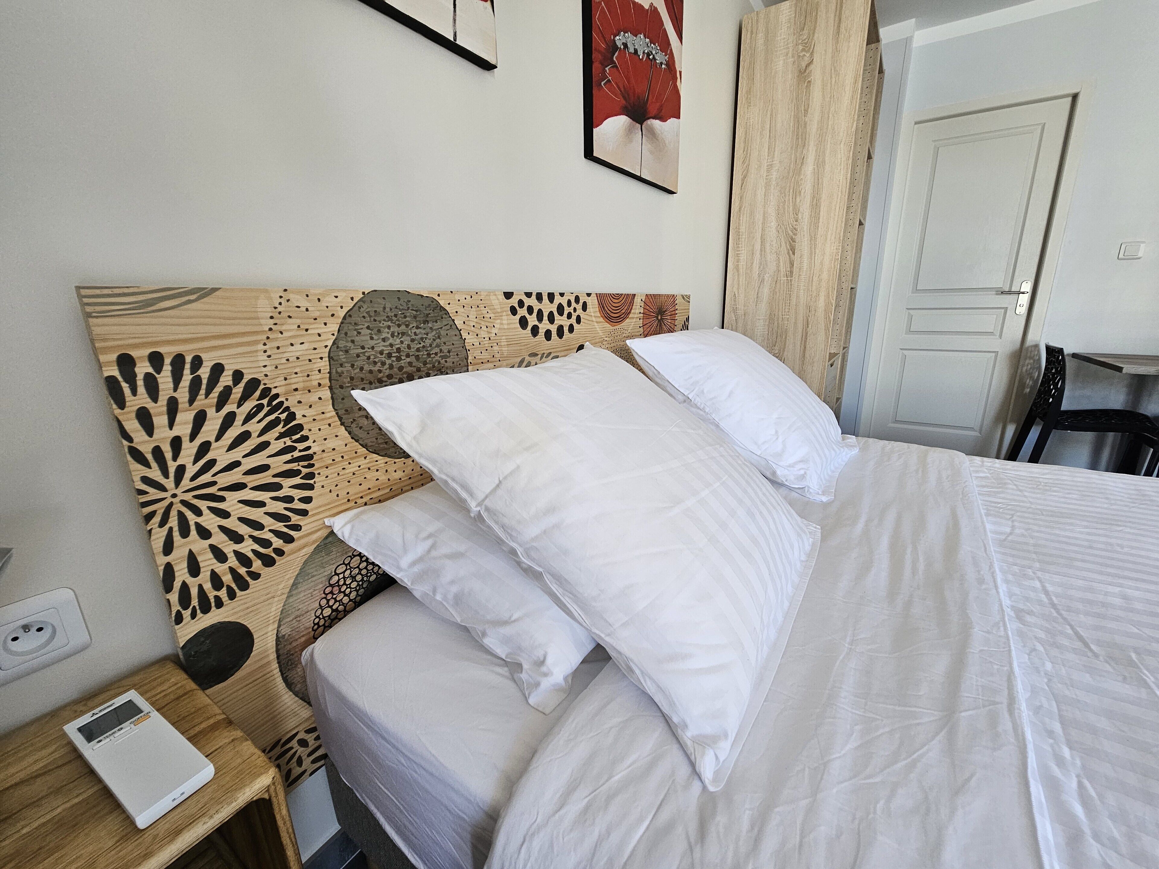Una cama bien hecha con ropa blanca, un cabecero de madera con un diseño decorativo y una mesita de noche con un distribuidor de corriente y un dispositivo.