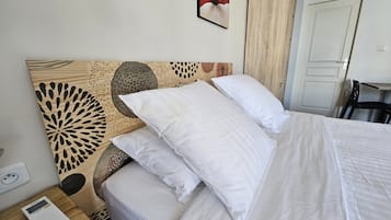 Una cama bien hecha con ropa blanca, un cabecero de madera con un diseño decorativo y una mesita de noche con un distribuidor de corriente y un dispositivo.